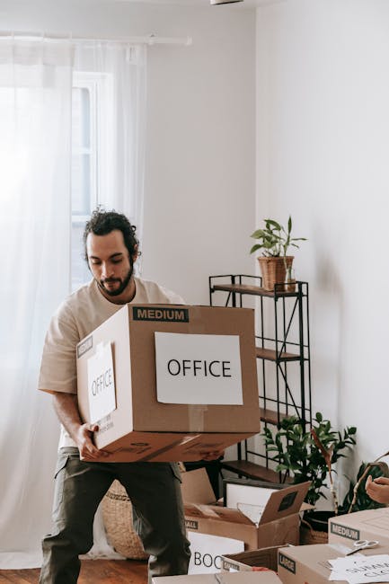 A professional removal worker from Man with Van Barnes Cray, dressed in dark work clothing, is inside a bright, spacious room with white walls and large arched windows letting in natural light. He is